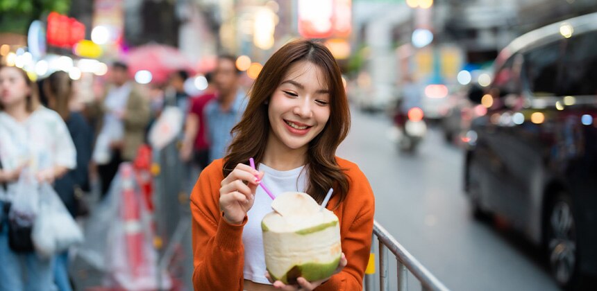 Woman smiles, holding a coconut drink on a busy street.