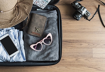 Open suitcase with travel items laid out on a wooden floor.